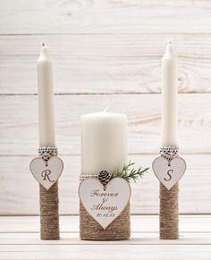 three white candles sitting next to each other on top of a wooden table with hearts