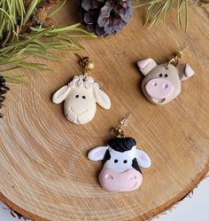 three farm animal key chains on top of a wooden table next to pinecone