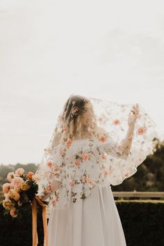 a woman in a white dress holding a flowered shawl over her head and looking off into the distance