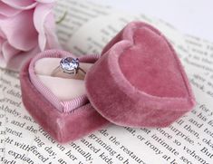 a pink heart shaped ring box with a diamond in it sitting on top of an open book