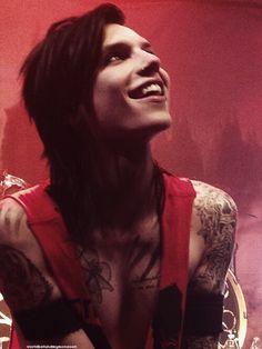 a man with tattoos and piercings on his chest is smiling while holding a guitar