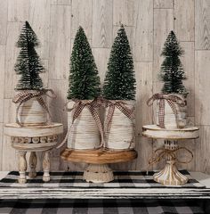 three small christmas trees are placed in buckets with twine ribbons on them, sitting on a table