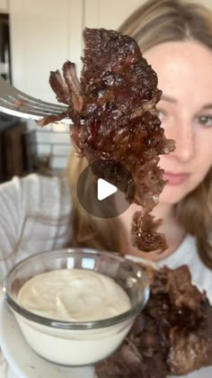 a woman is holding up some meat on a fork with ranch dip in front of her