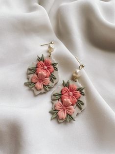 the earrings are decorated with pink flowers and green leaves on white fabric background, closeup