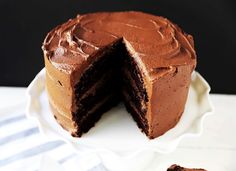 a chocolate cake with one slice cut out on a white plate and another piece is missing from the cake