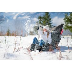 a woman is sitting in the snow with her hat on and she is throwing snow up into the air