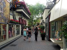 several people walking down the street in front of shops and buildings with flowers on them