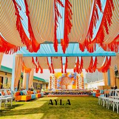 an outdoor wedding setup with orange and blue draping, white chairs, and red streamers