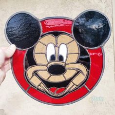 a hand holding up a mickey mouse face stained glass window ornament on a wall