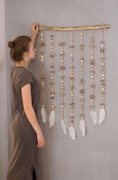 a woman standing in front of a wall hanging with white feathers and beads on it