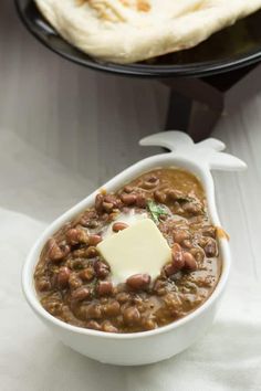 a white bowl filled with beans next to a pita bread on top of a table