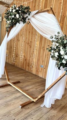 a wedding arch decorated with white flowers and greenery on the floor in front of a wooden wall