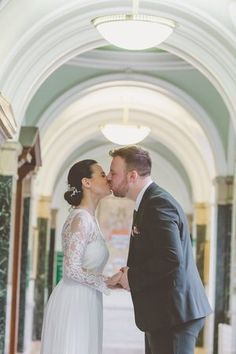 a bride and groom kissing in an ornate hallway at their wedding reception, with the bride wearing a long sleeved white dress