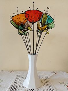 a white vase filled with colorful umbrellas on top of a doily covered table