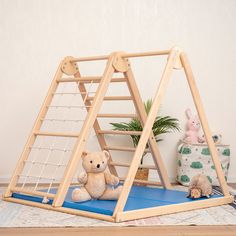 a teddy bear sitting on a mat in front of a wooden play set with a hammock