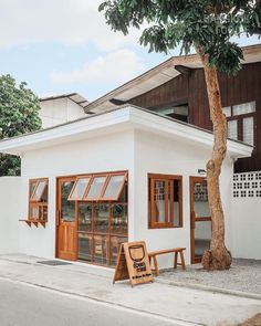 a small white building with wooden windows on the front and side, next to a tree