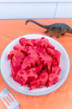 a white plate topped with red fruit next to a toy dinosaur on an orange table