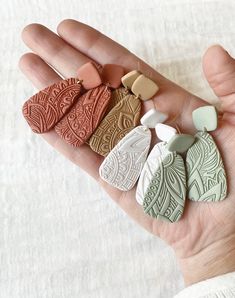 a person's hand holding five different colored clay pieces in their palm, with white linen behind them