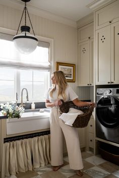 a woman standing in a kitchen holding a basket next to a washer and dryer