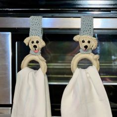 two white towels hanging from hooks in front of an oven with a dog on it