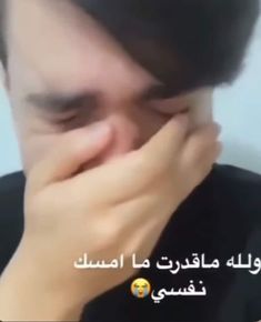 a man is covering his face with his hands while talking on the phone in arabic