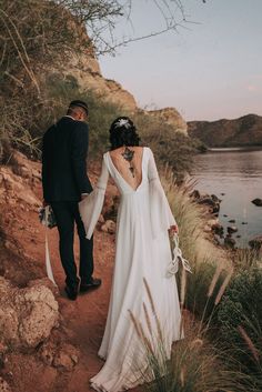 a bride and groom walking down a path by the water