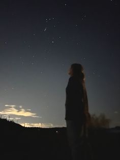 a woman looking up at the night sky with stars in the distance and clouds behind her