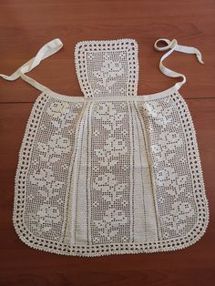 a white crocheted apron on top of a wooden floor next to a pair of scissors