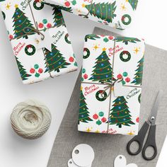 wrapping paper and scissors on a table with christmas tree designs, balls of twine