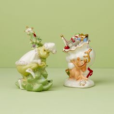 two ceramic figurines sitting next to each other on a green surface with white and gold trimmings