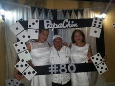 two women and one man are posing in front of a photo booth with dominos on it