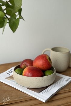 a bowl filled with fruit sitting on top of a wooden table next to a cup