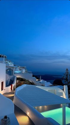 an outdoor swimming pool next to white buildings and trees at night with blue sky in the background