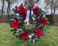 a wreath with poinsettis and pine cones on a stand in the grass