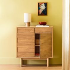 a wooden cabinet sitting next to a lamp on top of a hard wood floor in front of a yellow wall