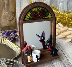 a small mirror with two cats on it and some flowers in front of the mirror