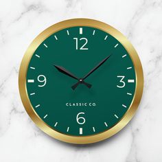 a green and gold clock sitting on top of a white marble countertop with the numbers twelve o'clock