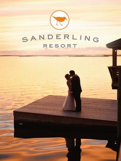 a bride and groom standing on a dock in front of the sun setting at sanderling resort