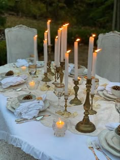 a table topped with lots of white plates and glasses filled with lit candles next to each other