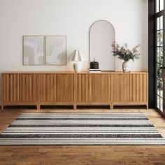 a room with a rug, mirror and two vases on the sideboard in front of it