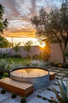 the sun is setting over an outdoor garden with water fountain and wooden benches, surrounded by succulents