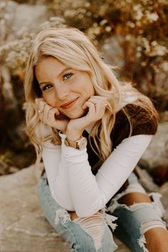 a beautiful blonde woman sitting on top of a rock