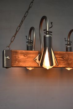 a wooden light fixture with three lights hanging from it's sides and an iron chain on the side