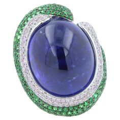 Tanzanite Oval Cabochon 50.00 Carats Dark Sea Blue Color & Hues Tsavorites 1.25 ctw Diamonds 1.25 ctw 18K White Gold 26.80 grams Ring Size 7 31.50 mm length of front ring 24.00 mm width of front ring 7.50 mm back shank width Sea Blue Color, Dark Sea, Blue Tanzanite, Unique Ring, Sea Blue, Gem Stone, Oval Cabochon, Blue Sea, Cocktail Rings