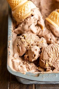 two scoops of ice cream in a blue container on a wooden table with three cones