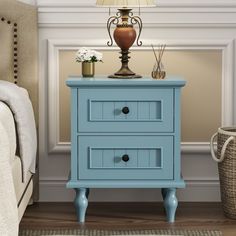 a blue nightstand with two drawers and a lamp on top in a room next to a bed