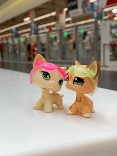 two little pony dolls sitting next to each other on a white table in front of a store