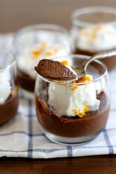 four desserts in small glass dishes with spoons on the side and one is topped with whipped cream, orange zest, and chocolate