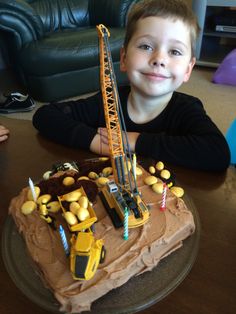 a young boy sitting in front of a birthday cake with construction vehicles on it and candles