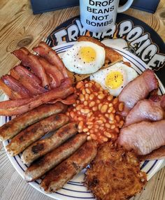 a breakfast plate with bacon, eggs, beans and ham on it next to a coffee mug